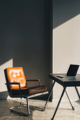 Minimalist workspace featuring a modern leather chair and laptop. The sunlight streams in, casting long shadows, creating a serene and productive environment. Generative AI