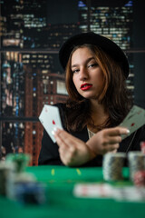 Fototapeta premium attractive girl in jacket and hat holding poker cards and looking at camera in casino. a woman deals cards
