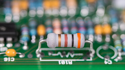 Closeup a white resistor with standard colored code on green printed circuit board. Electronic components with color band system on PCB with beautiful bokeh in blur background. Electrical engineering.
