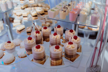 A dessert table with a variety of desserts including cakes and cupcakes. The desserts are arranged on a glass platter and are topped with cherries. The table is set up for a party or event