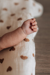 Cute little hand of newborn baby on muslin swaddle with hearts, aesthetics children's lifestyle