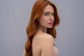 Fototapeta premium Cute young woman with long ginger hair on a grey background