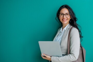Joyful female entrepreneur in casual business attire, holding a laptop, smiling confidently. Portrait on solid teal background. Ideal for small business promotions, coaching services, financial.