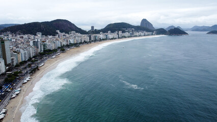 Visão aérea da praia de Copacabana, Rio de Janeiro, em um dia nublado com nuvens no céu. A imagem captura a beleza única da cidade com a famosa praia e o mar do oceano atlântico © RNL Fotografia