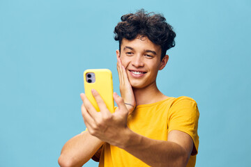 Young man smiling while taking a selfie on a bright blue background, showcasing joy and confidence...