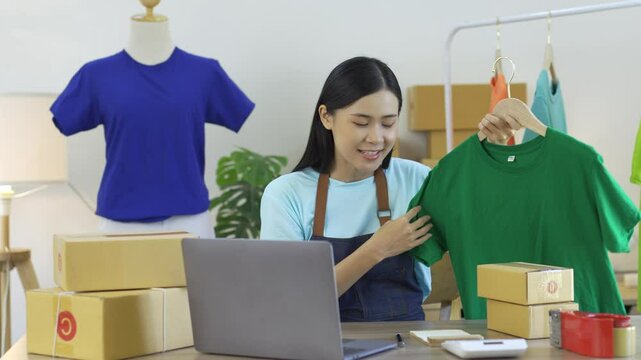 Asian sme businesswoman live streams while selling a green t shirt using a laptop computer for her online store