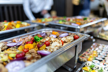 A chafing dish filled with grilled chicken, red onions, and vegetables is ready for guests at a catered event