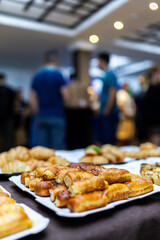 A variety of baked goods displayed on a table at a bustling event with people mingling in the background