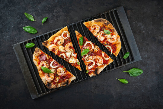 Traditional Italian pinsa bread prosciutto e salsa di pomodoro sliced with seafood, buffalo mozzarella and tomato sauce served as top view on a rustic cast iron grillage