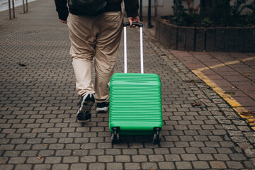 Unrecognizable man pulling green suitcase outdoors. Rear view. Copy space. Man walking on the...
