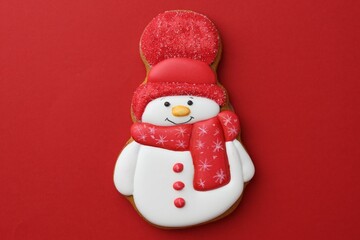 Tasty Christmas cookie in shape of snowman on red background, top view