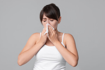Woman with napkin suffering from sinusitis on grey background