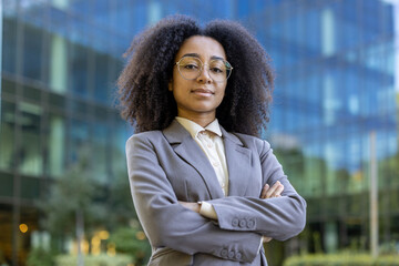 Confident African American businesswoman standing outside modern glass office building. Her...