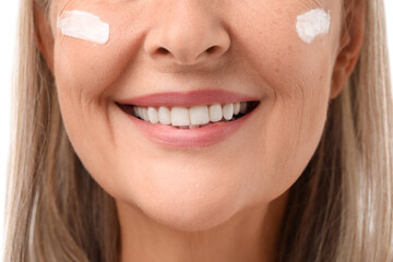 Senior woman with face cream on white background, closeup
