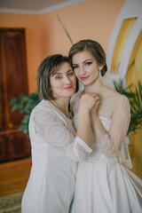 A bride is standing in front of a wedding dress, touching it and adjusting it. The dress is white...
