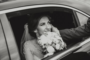 A bride is sitting in a car with a bouquet of flowers. She is smiling and she is happy