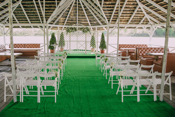 A large open space with a green carpet and white chairs. The chairs are arranged in rows and there is a stage in the middle