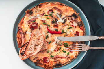 Italian frittata or omelette with tomatoes, cheese and toast on a blue plate with cutlery and napkin. Healthy breakfast concept. Close-up. Selected focus.