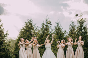 A group of women are throwing flower petals in the air. The bride is in the center of the group,...