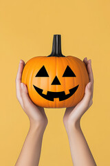 hands holding carved pumpkin on plain yellow  background 