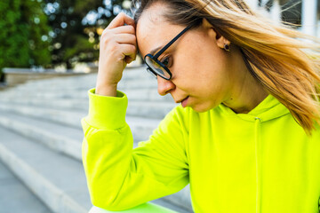 A young woman in a vibrant hoodie contemplates while sitting on outdoor steps during the day