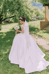 A woman in a white dress is walking in a field with a bouquet of flowers. She is wearing a veil and a white wedding dress