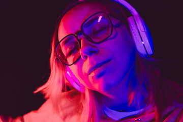 The woman closes her eyes, lost in the rhythm of music while wearing oversized headphones,...