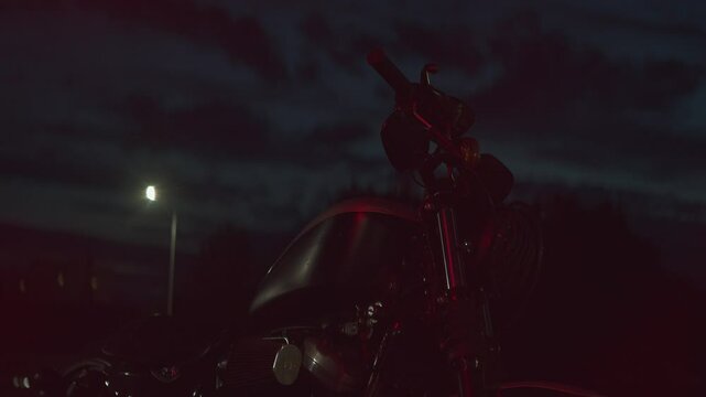 Close-up of motorcycle parked at night in patch of reflected of red light. Slow motion. Motorcycles have become not only means of transportation, but also eal symbol of freedom, speed and adventure