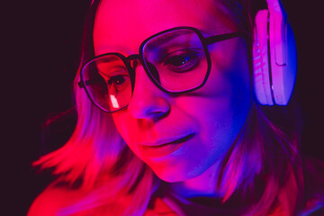 A woman with glasses and headphones enjoys music in vibrant colors during a night setting