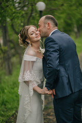 A man and a woman are kissing each other. The man is wearing a blue suit and the woman is wearing a white dress