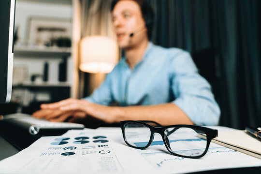 Call center consulting with customers on headphones on monitor in business paragraph with typing on pc with dynamic data marketing analysis planning at modern home office at night time. Pecuniary.