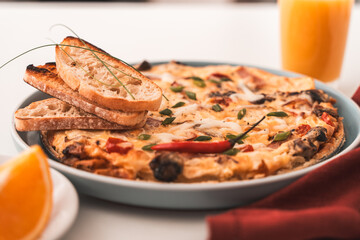 Italian frittata or omelette with tomatoes, cheese and toasted toast on a blue plate with a napkin on a white table and a glass of orange juice. Healthy breakfast concept. Selected Focus