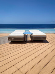Two sun lounger on a patio infront of a swimming pool against blue water of Atlantic Ocean and blue sky