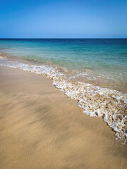 Sandy Atlantic Ocean beach with soft waves against turquoise and blue water and blue sky