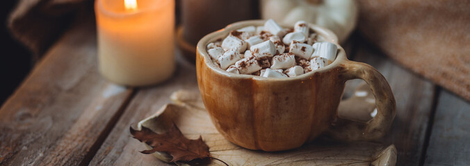 Spicy sweet fall hot drink: delicious pumpkin latte with cinnamon, marshmallow with salted caramel. Served in handmade artisan mug in shape of pumpkins, cozy home decor with candles, dry autumn leaves
