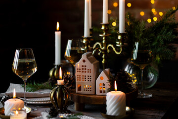 Beautiful table setting for family Christmas dinner at home. Cozy atmosphere, candlelight. Wine glasses, vintage chandelier, elegant interior. Fir tree branches, wooden furniture, dark, bokeh