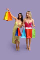 Beautiful young women with shopping bags on purple background