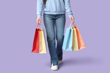 Young woman with shopping bags on lilac background