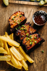 Close-up of barbecue ribs with crispy fries on a wooden board, served with a side of dipping sauce