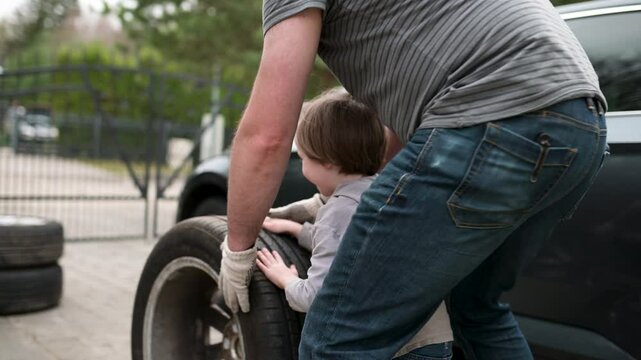 Cute toddler boy helping his father to change car wheels in their backyard. Father teaching his little son to use tools. Active parent of a small child. Slow motion summer day footage.