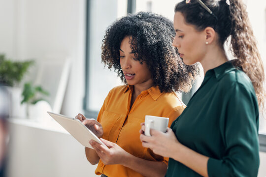 Two smart pretty business women taking a break while cheaking her digital tablet standing in the office