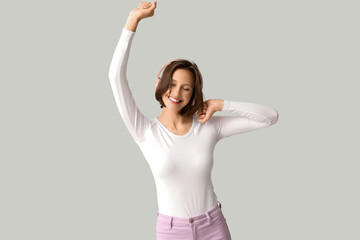 Happy young woman in modern headphones listening music on grey background