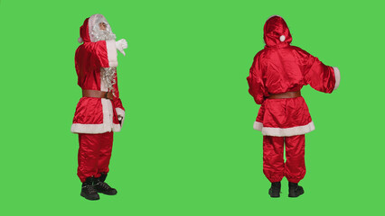 Saint nick shows thumbs down on camera, feeling displeased and expressing disappointment against full body greenscreen. Santa claus character doing dislike gesture in frustration.