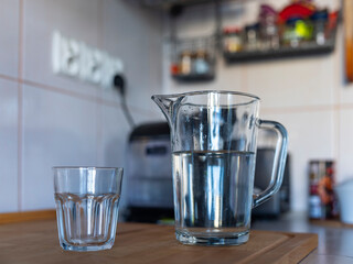 A glass jug of water and a glass standing on the kitchen counter.