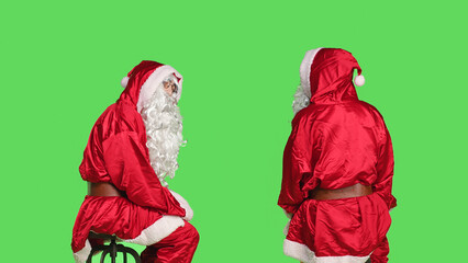 Saint nick sitting on chair posing over greenscreen backdrop, santa claus embodiment in red and...