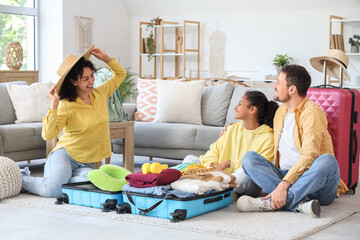 Happy family sitting on floor and packing suitcase for travel at home