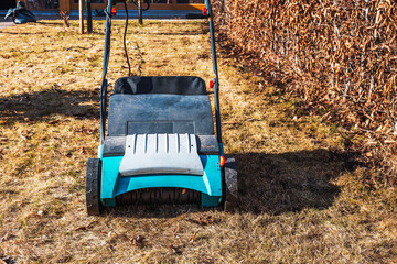 Electric lawn scarifier on dry grass next to hedge in spring garden during lawn maintenance. Sweden.