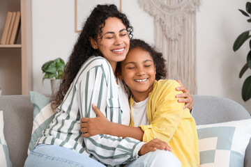 Happy young African-American woman with her daughter sitting on sofa and hugging at home