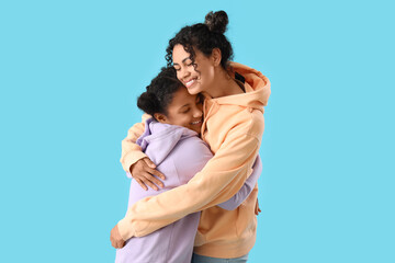 Happy young African-American woman with her daughter hugging on blue background