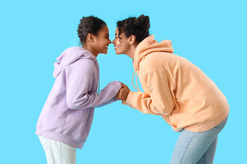 Young African-American woman with her daughter touching noses on blue background
